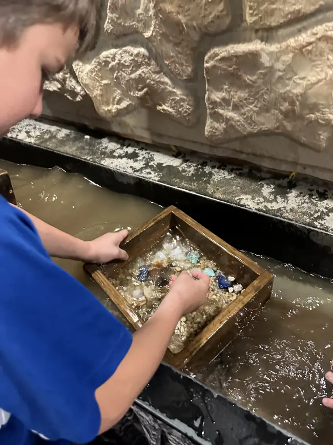 Student using a wooden tray to sift stones in water