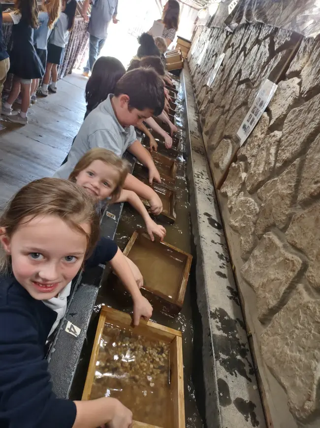 Students using wooden sifting trays along a water trough