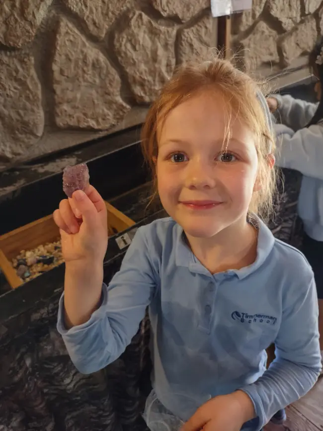 Student holding up a purple stone beside the water trough