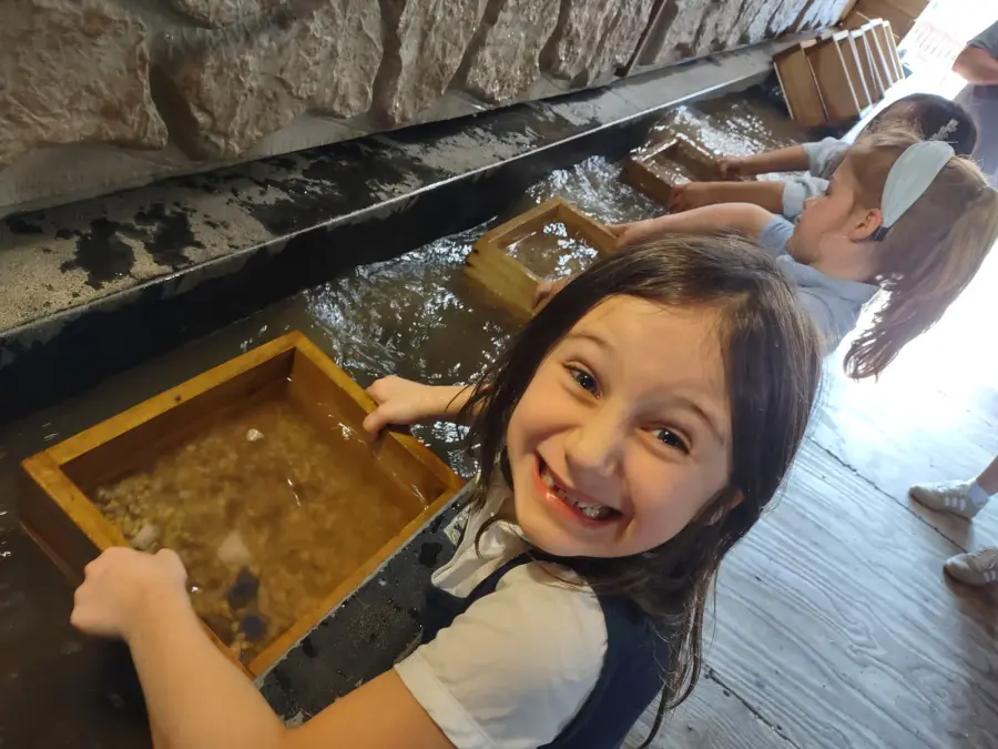 Student sifting stones in a wooden tray at a water trough